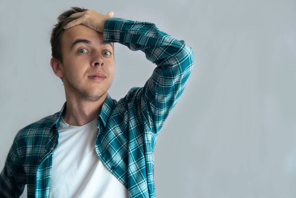 Portrait of a shocked young guy. A man in a casual shirt holds his hand on forehead. Pleasant surprise, expression. Copy Space - Foto, afbeelding