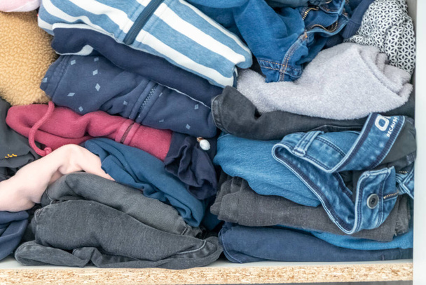 Chaotic wardrobe and sloppy closet shows many outfits of a woman with shopping addiction and many clothes like pullovers, shirts and trousers as crumpled laundry stored into a messy heap of fashion - Foto, Imagen