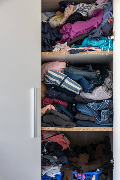 Chaotic wardrobe and sloppy closet shows many outfits of a woman with shopping addiction and many clothes like pullovers, shirts and trousers as crumpled laundry stored into a messy heap of fashion - Foto, Imagen