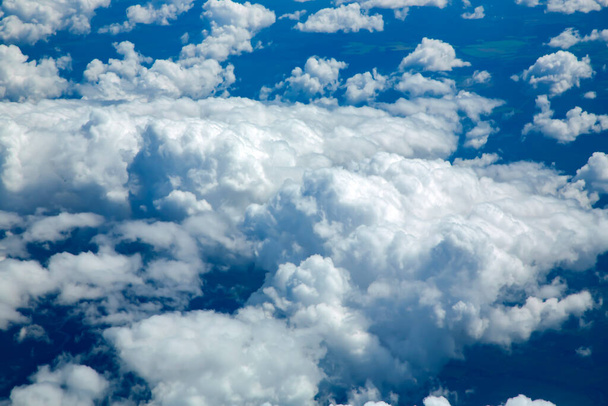 Aerial view from airplane window on the white fluffy clouds in the blue sky. Beautiful vast blue sky with amazing scattered cumulus clouds. - 写真・画像