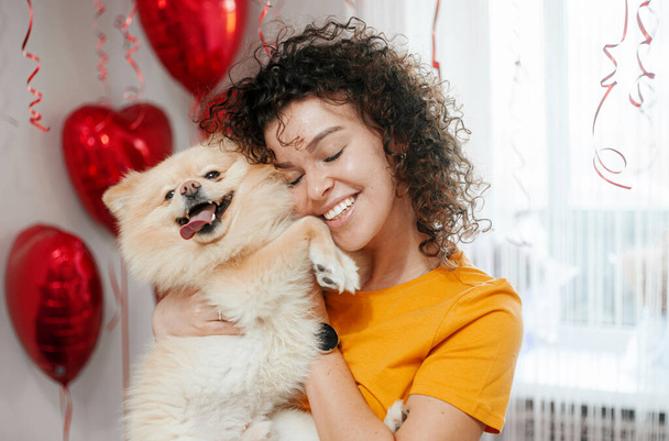Σγουρά μαλλιά γυναίκα παίζει με το σκυλί της στο σπίτι. - Φωτογραφία, εικόνα