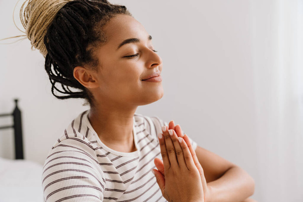 Young black woman with pigtails smiling while meditating at home - Фото, зображення
