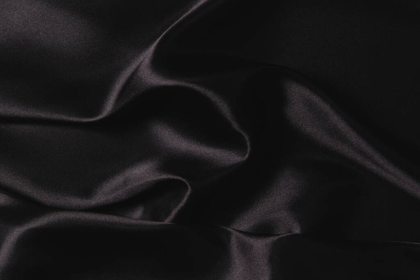 Abstract monochrome elegant luxury cloth background. Black color background with drapery and wavy folds of luxurious silk satin material. Top view. - Фото, изображение