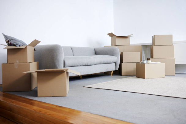 Tiro de cajas de cartón y un sofá en una sala de estar vacía durante el día. - Foto, imagen