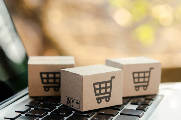 Online winkelen. Kartonnen doos met een winkelwagen logo op laptop toetsenbord. Shopping service op het online web. aanbiedingen levering aan huis - Foto, afbeelding