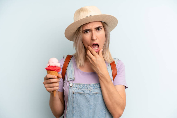 blonde woman with mouth and eyes wide open and hand on chin. ice cream and summer concept - Fotó, kép