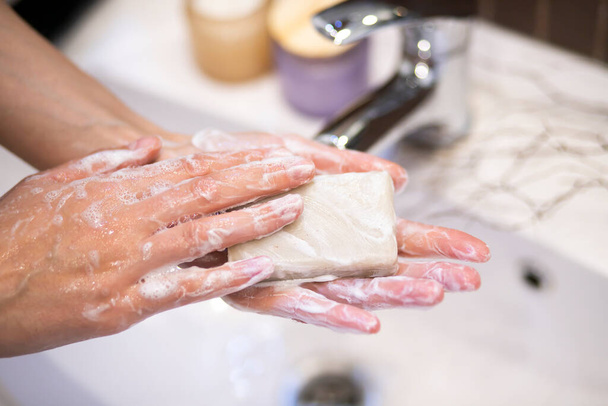female hands hold soap and wash their hands with water on the bathroom white soap - Фото, изображение