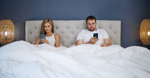 Shot of a young couple using their phones separately after an argument in bed. - Zdjęcie, obraz