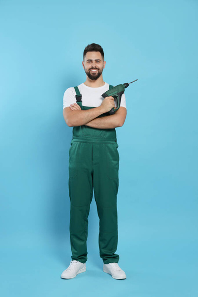 Young worker in uniform with power drill on light blue background - Foto, imagen