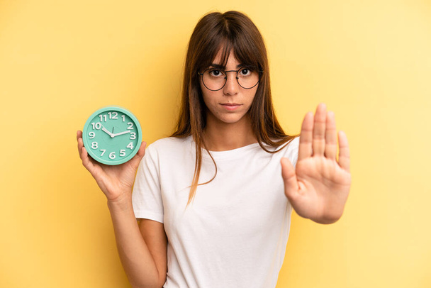 hispanic woman looking serious showing open palm making stop gesture. alarm clock concept - Zdjęcie, obraz