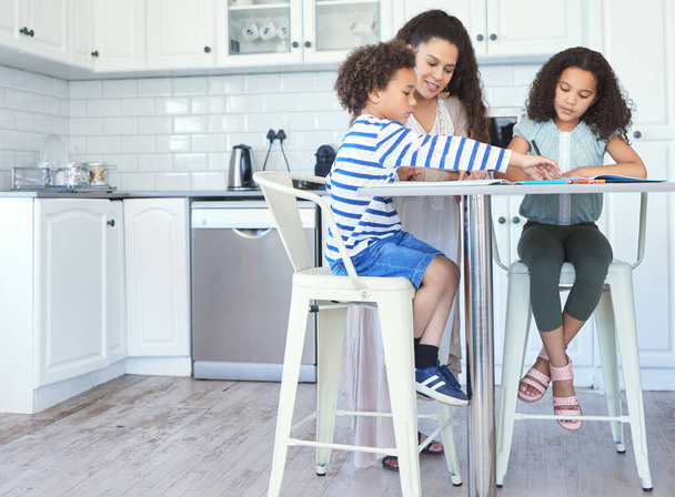 Aufnahme einer Mutter, die ihren Kindern bei den Hausaufgaben am Küchentisch hilft. - Foto, Bild