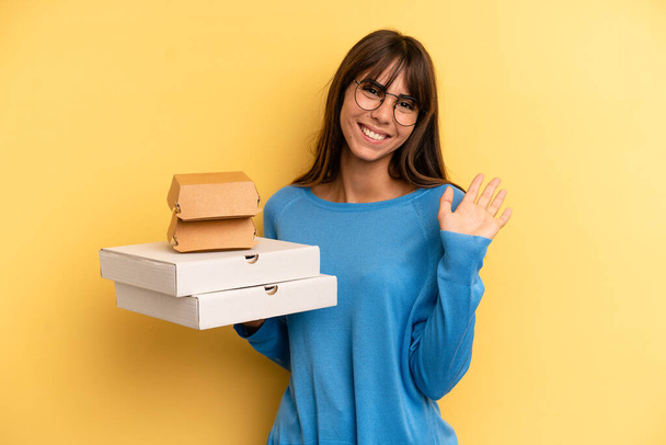 pretty woman smiling happily, waving hand, welcoming and greeting you. take away fast food concept - Zdjęcie, obraz
