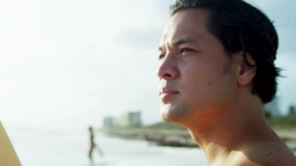 Мужчина держит доску для серфинга на пляже
 - Кадры, видео