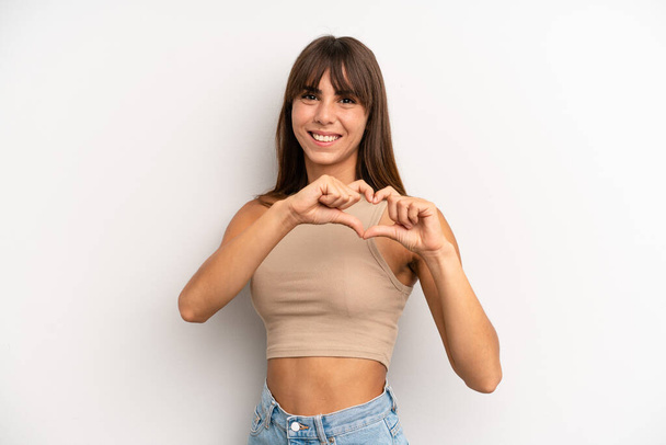 hispanic pretty woman smiling and feeling happy, cute, romantic and in love, making heart shape with both hands - Valokuva, kuva