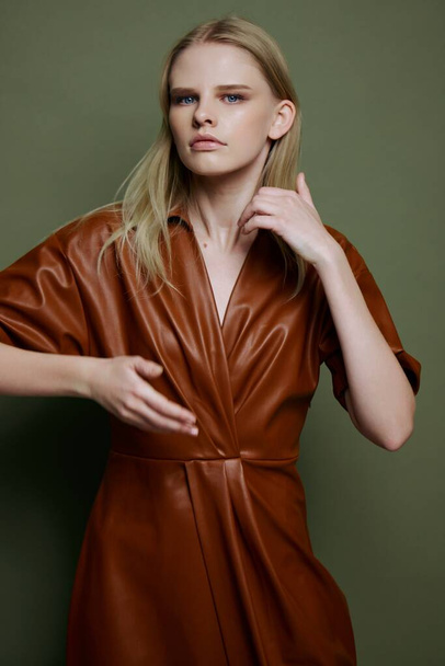 Крутой портрет в студии со стильной профессиональной блондинкой-моделью в модном кожаном платье. Студийные фонограммы на оливковом фоне. Высокое качество фото - Фото, изображение
