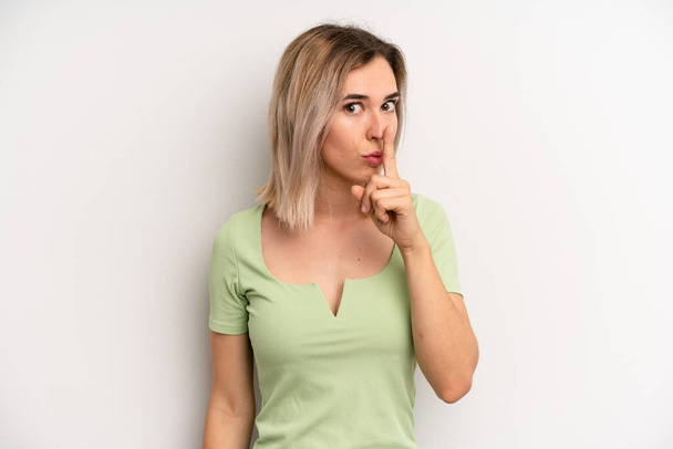 young adult blonde woman asking for silence and quiet, gesturing with finger in front of mouth, saying shh or keeping a secret - Foto, afbeelding