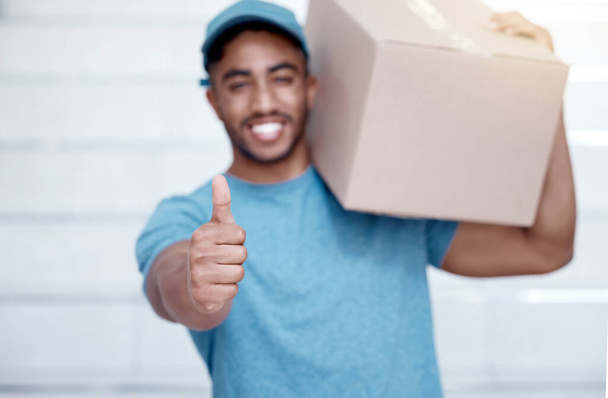 Portrait of a young delivery man showing thumbs up while holding a box. - Foto, immagini