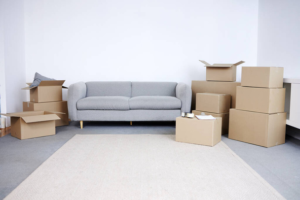 Знімок картонних коробок і диван у порожній вітальні протягом дня
. - Фото, зображення