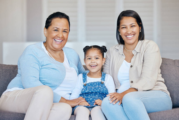 Happy mature grandmother relaxing with her granddaughter and adult daughter at home. Cheerful little hispanic girl sitting on the couch together with her mother and grandmother. - Foto, Imagen