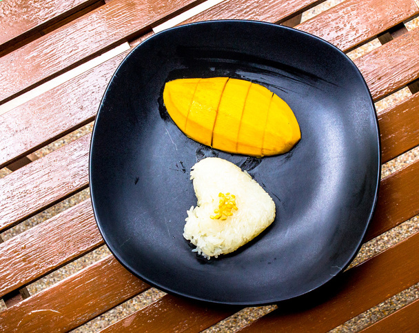 Kalp işareti tatlı yapışkan pirinç ve mango içinde siyah yuvarlak yüzey. - Fotoğraf, Görsel