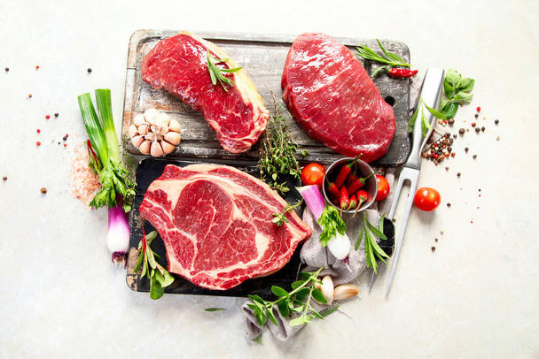 Fresh raw beef meat to make delicious juicy steaks with spices and herbs. Preparation for grilled meat on white background, top view. - Foto, Bild