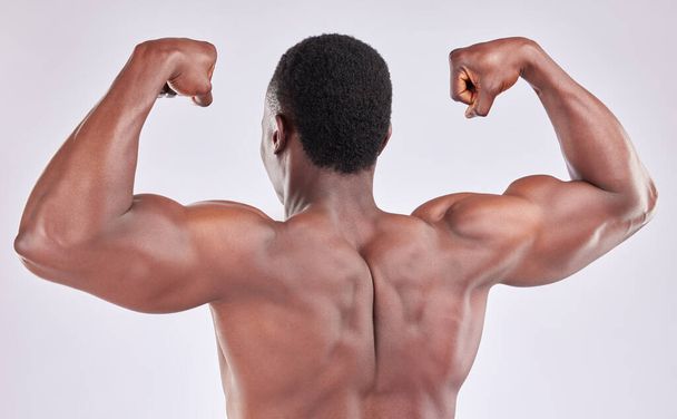 Studio shot of muscular young man flexing his arms against a grey background. - Foto, afbeelding