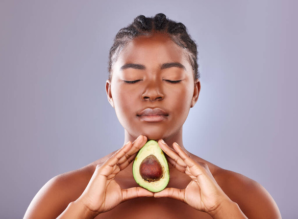 Studio shot of a beautiful young woman holding a halved avocado. - Foto, afbeelding