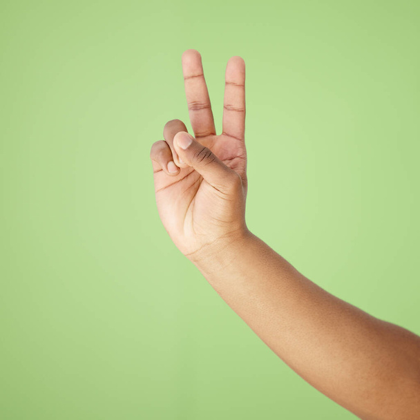 Cropped shot of a hand showing the peace sign against a green background. - Foto, Bild