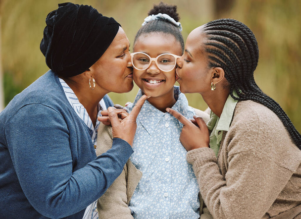 Cropped portrait of an adorable little girl being kissed on the cheeks by her mother and grandmother. - Zdjęcie, obraz