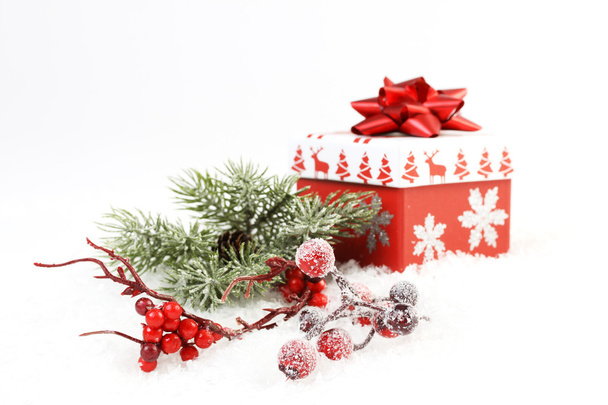 Ijsvorming pine tak en tak met rode rowanberries en rose heupen en geschenkdoos met sneeuwvlokken en kerstbomen en rendieren en rode mat strik op sneeuw - Foto, afbeelding