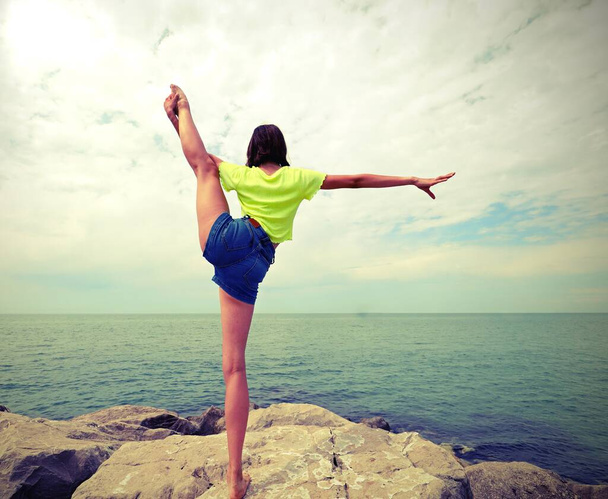 молодая стройная девочка делает упражнения у моря со старым тонизирующим эффектом - Фото, изображение