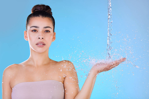 Aufnahme einer schönen jungen Frau, die vor blauem Hintergrund mit Wasser bespritzt wird. - Foto, Bild