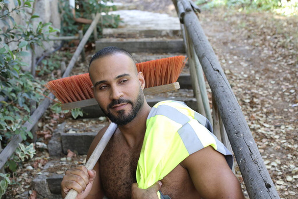 close-up portrait of handsome shirtless young man with reflective vest and broom in park outdoors - Zdjęcie, obraz