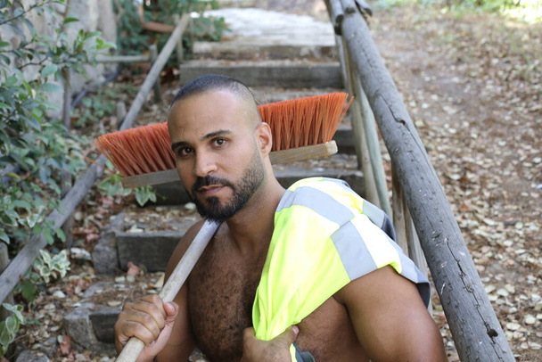 close-up portrait of handsome shirtless young man with reflective vest and broom in park outdoors - Foto, Imagem