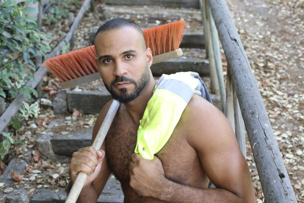 close-up portrait of handsome shirtless young man with reflective vest and broom in park outdoors - Foto, immagini