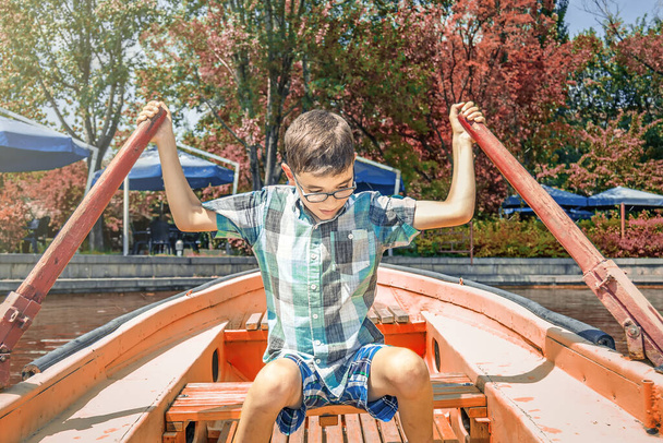 A boy in glasses sails on a boat and rowing with oars - 写真・画像