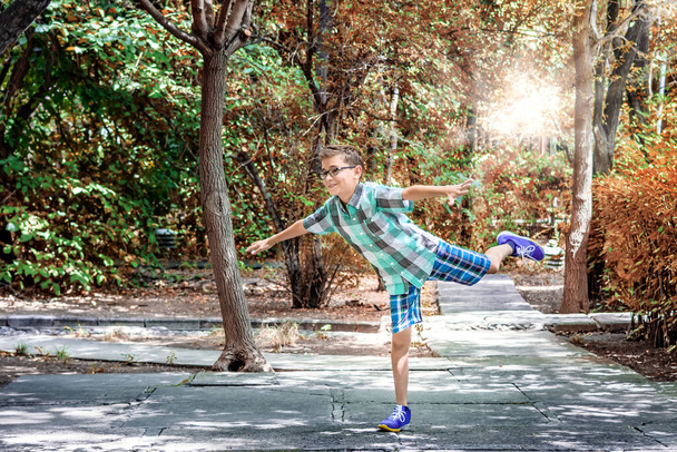 Alegre, alegre y feliz adolescente en pantalones cortos de pie en una pierna en el parque - Foto, Imagen