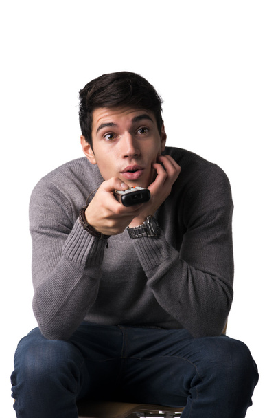 Attractive young man holding remote control and changing TV channels - Photo, image