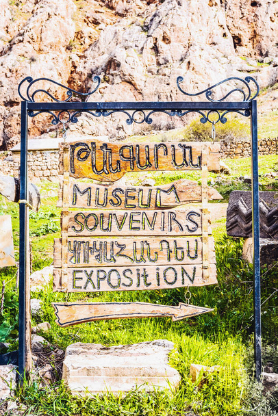 Vintage style wooden signboard and arrow in English and Armenian indicating the direction to the exhibition, museum and souvenirs on a mountain background - Foto, Bild