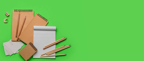 Notebooks with pencils, paper notes and sharpener on green background with space for text - Photo, image