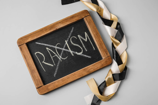 Chalkboard with crossed out word RACISM and braided ribbons on grey background - Foto, immagini