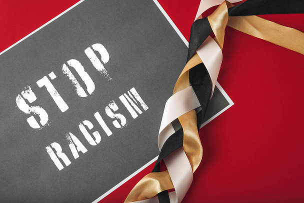 Braided ribbons and paper sheet with text STOP RACISM on color background - 写真・画像