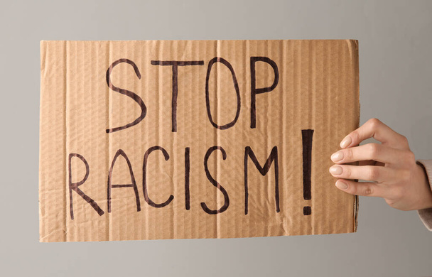 Χέρι κρατώντας κομμάτι του χαρτοκιβωτίου με κείμενο STOP RACISM σε γκρι φόντο - Φωτογραφία, εικόνα