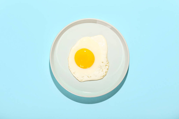 Plate with fried egg on blue background - Fotoğraf, Görsel