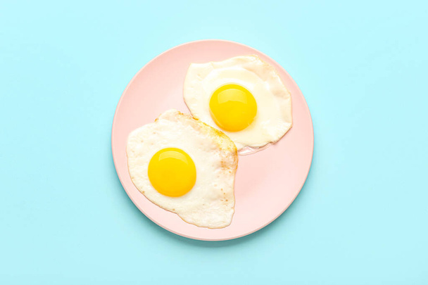 Plate with tasty fried egg on blue background - Foto, afbeelding