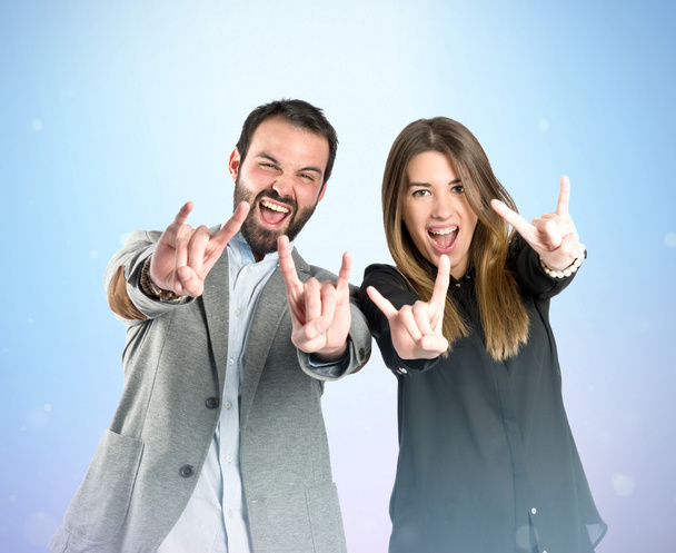 Couple doing the horn sign over gloss background  - Фото, зображення