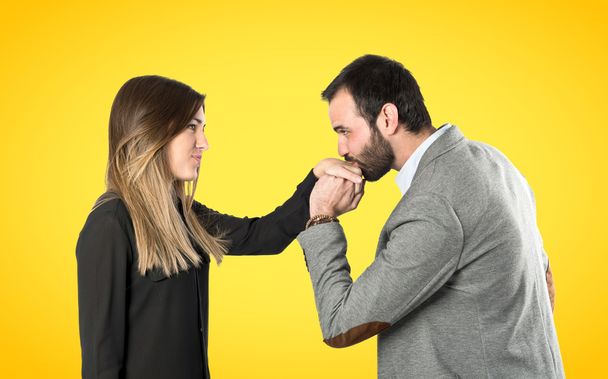 mężczyzna całuje kobietę w rękę na żółtym tle.  - Zdjęcie, obraz