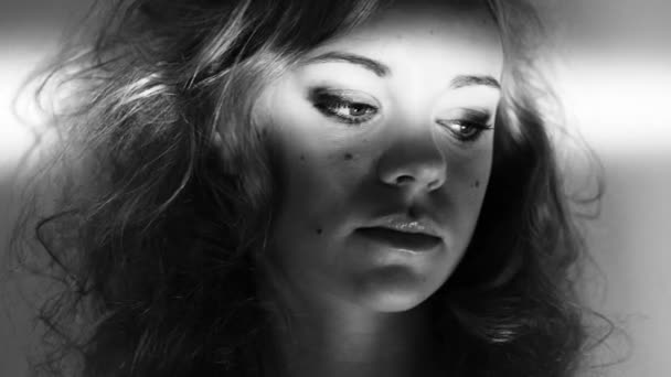 Black and white 4k video footage of a beautiful young woman standing against a wall with a light shinning over her eyes. - Séquence, vidéo