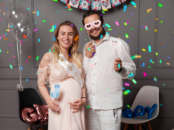 Happy couple holding balloons with inscription boy or girl during gender reveals party, over confetti and balloons. - Photo, Image