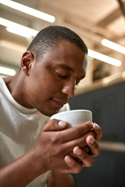 Cropped of professional male barista snif fresh aromatic natural coffee in cup. Young focused black man with closed eyes checking and studying coffee flavor. Coffee process making. Small business - Fotoğraf, Görsel